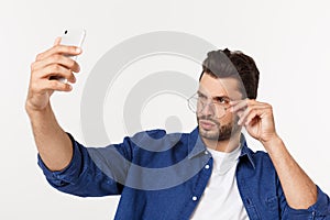 Portrait of an attractive young man taking a selfie while standing and pointing finger isolated over white background.