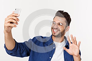 Portrait of an attractive young man taking a selfie while standing and pointing finger isolated over white background.