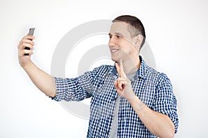 Portrait of an attractive young man taking a selfie while standing and pointing finger isolated over white background. Photo of a
