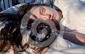 Portrait of an attractive, young, sexy, seductive dark brown haired woman in Bed, snowflakes on her long hair