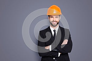 Portrait of attractive young stylish investor with stubble in orange hard hat and black tux, tuxedo with tie, looking at