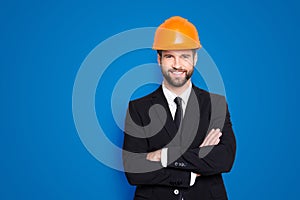 Portrait of attractive young stylish investor with stubble in orange hard hat and black tux, tuxedo with tie, looking at