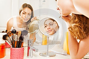 Young woman apply makeup, seen in bathroom mirror