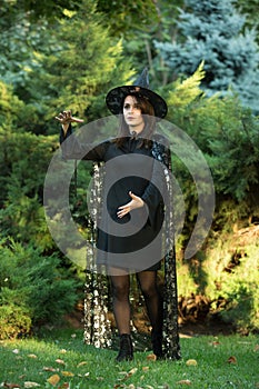 Portrait of an attractive young woman in a black dress with a cape on a background of green forest