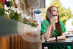 Portrait of attractive young woman enjoying tasty cup of coffee sitting at table in outdoor cafe terrace in summer day.