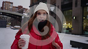 Portrait of attractive young woman influencer in warm winter clothes holding cup with coffee recording video blog