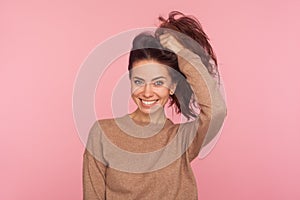 Portrait of attractive young woman in pullover making ponytail with long brown hair and smiling at camera