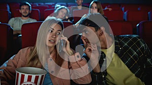 Portrait of attractive young woman talking on the phone, annoying audience and her boyfriend while watching film at the
