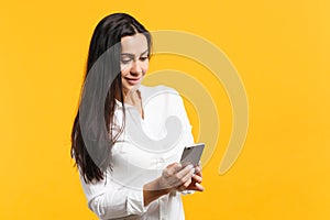 Portrait of attractive young woman in white casual shirt using mobile phone and typing sms message  on yellow