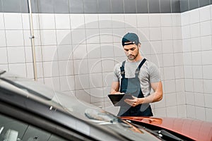 portrait of auto mechanic with notepad examining car