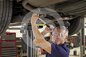 Portrait Of Auto Mechanic Working Underneath Car In Garage