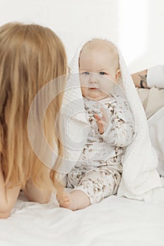 Portrait of awesome blue-eyed plump baby infant covered with white cotton blanket sitting on bed linen with parents.