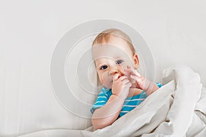 Portrait of baby 11 months old on bed close up. Funny kid on white cloth smiles. Restful sleep concept, teething, baby care.