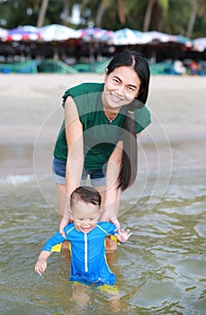 Portrait of baby boy playing water on sea with mother holding