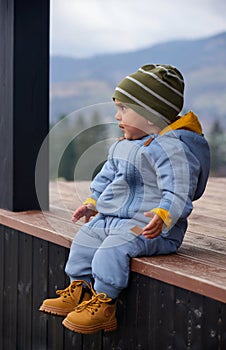 Portrait of a baby boy sitting on wooden patio while looking at the view
