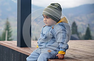 Portrait of a baby boy wearing warm blue overall sitting outdoor and looking at view