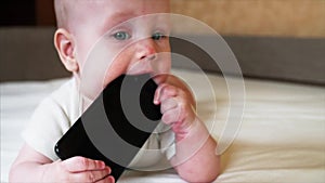 Portrait of baby boy who is chewing and sucking black smartphone