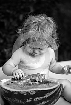 Portrait of baby child outdoors. One year old baby boy eating watermelon slice in the garden.