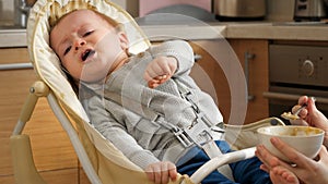 Portrait of baby crying and refusing to eat in highchair at kitchen. Concept of parenting, healthy nutrition and baby feeding