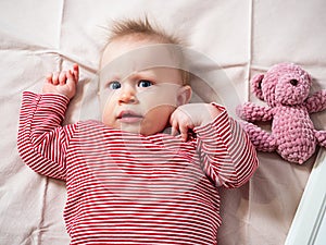 Portrait of a baby girl, 8 months old, playing with a soft toy, top view, close-up. A mischievous, beautiful girl with fair skin