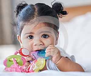 Portrait, baby girl and biting toys in bedroom, house and home for development, growth and teething progress. Cute kid