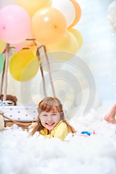 Portrait of a baby girl lying on a cloud next to a basket of balloon in the clouds, traveling and flying in dreams