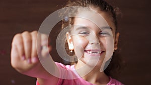 Portrait of a baby girl with a toothless smile. Shows a ripped tooth into the camera in an extended hand. Shift focus