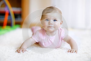 Portrait of baby girl in white sunny bedroom. Newborn child learning crawling.