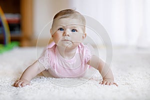 Portrait of baby girl in white sunny bedroom. Newborn child learning crawling.