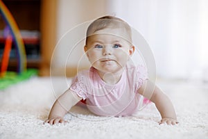 Portrait of baby girl in white sunny bedroom. Newborn child learning crawling.