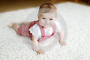 Portrait of baby girl in white sunny bedroom. Newborn child learning crawling.