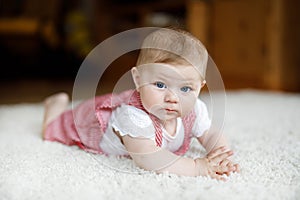 Portrait of baby girl in white sunny bedroom. Newborn child learning crawling.