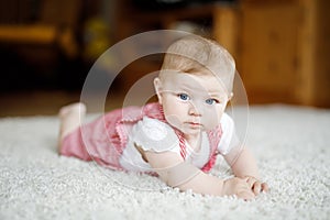 Portrait of baby girl in white sunny bedroom. Newborn child learning crawling.