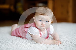 Portrait of baby girl in white sunny bedroom. Newborn child learning crawling. Nursery for children. Textile and bedding