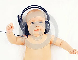 Portrait baby listens to music in headphones lying on the bed