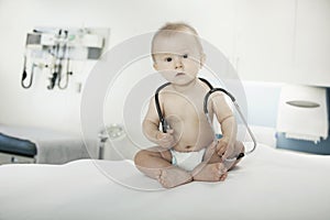 Portrait of baby sitting on an examination table in the doctors office with a stethoscope around his neck