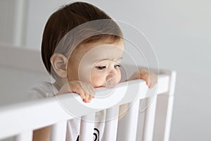 Portrait of baby staying in his baby cot looking sadly