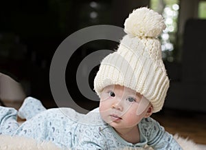 Portrait of a baby in a winter hat crawling on a sheep rug. Cute caucasian baby with dark eyes portrait