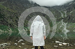 Portrait from back of person in white raincoat on background of beautiful lake on top of mountain. Background. Man hiking in the