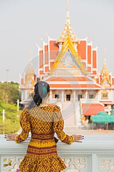 Portrait back side Asian woman in a yellow Thai patterned standing in front of a Buddhist Chruch while traveling in Asia