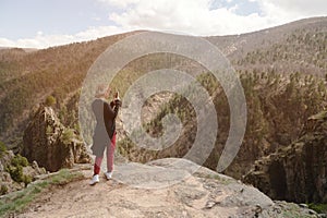 Portrait from the back of a traveling girl taking pictures of an epic landscape with rocks on her smartphone