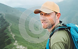 Portrait of backpacker man in baseball cap walking by the foggy cloudy weather mountain range path with backpack. Active sports