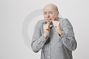 Portrait of bald funny man with a beard holding his fists up standing in defensive pose. Guy is afraid and terrified