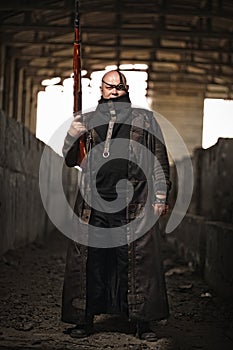 Portrait of a bald man from post-apocalyptic world with rifle in leather clothing as style Fallout or Mad Max