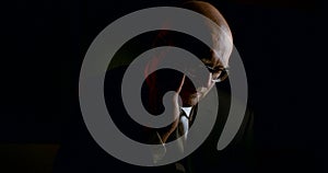 Portrait of a bald sad man in glasses and a business suit with a tie, it is on a black background. He charges the gun