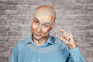 Portrait bald sad man thinks about money and a small salary. White bald guy in blue shirt on brick wall background showing thumbs