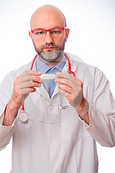 Portrait of bald slim doctor wearing white uniform, blue shirt, red stethoscope and glasses on white background. Caucasian in 40s