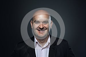 Portrait of a bald smiling, affable man in a suit against a dark background