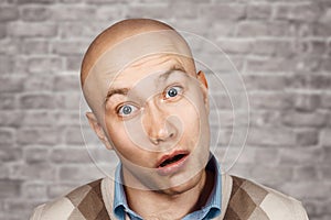 Portrait of a bald stupid surprised guy with open mouth on an brick wall background photo