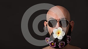 Unshaven man with beard with flowers and sunglasses on dark background with copyspace